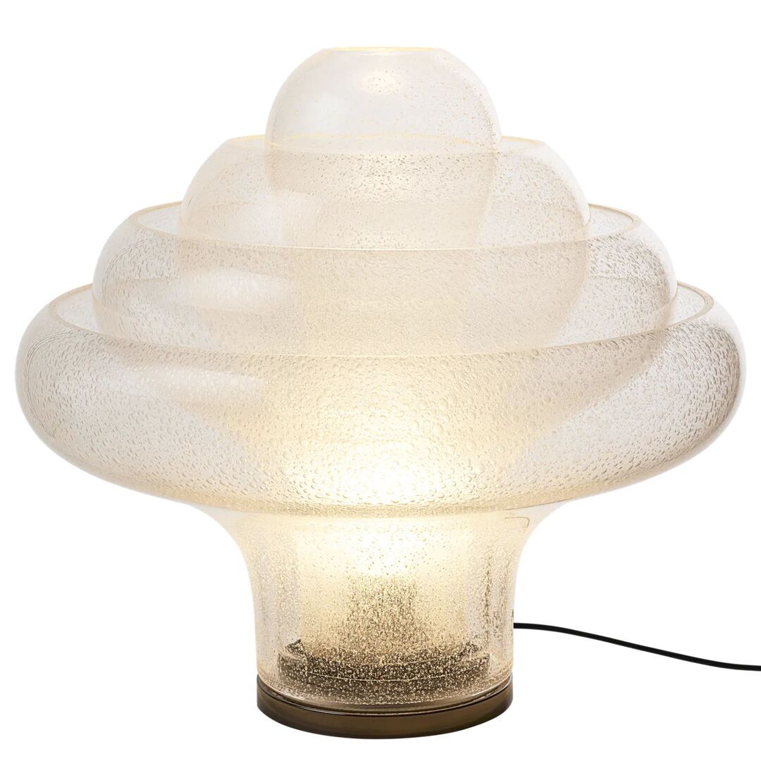 Glas als Kunst. Licht als Stimmung.  Die Lotus Tischleuchte von Carlo Nason – 1969 entworfen und nach mehr als 50 Jahren von GUBI neu aufgelegt – ist ein Meisterwerk der Murano-Glaskunst. Vier ineinander verschachtelte, mundgeblasene Glasschirme bilden eine konzentrische, blütenartige Struktur, die schon ohne Licht endlos fasziniert. Hergestellt mit der historischen «Pulegoso»-Technik aus den 1920er-Jahren, bei der winzige Luftblasen ins Glas geblasen werden, erhält jedes Stück eine halbtransparente Textur, die Tiefe und Lichtstreuung auf einzigartige Weise verstärkt – und jede Leuchte zum Unikat macht.  Eingeschaltet erzeugt die Lotus ein sanftes, diffuses Leuchten ganz ohne Blendung oder sichtbare Lichtquelle – pure Atmosphäre, die jedem Raum Ruhe und Wärme verleiht. Nur die erfahrensten Murano-Glasbläser sind in der Lage, Stücke dieser Grösse und Komplexität zu schaffen. Das Ergebnis ist eine Leuchte, die weit mehr ist als Beleuchtung – sie ist ein Kunstwerk.
